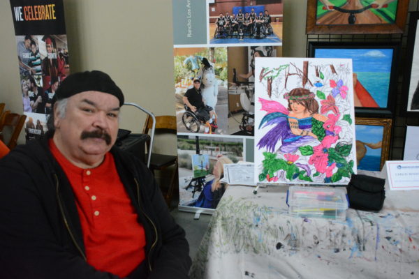 Carlos sits next to a coloring book representation of one of his works which children can color