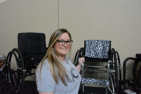 Brooke Everett smiles next to smaller wheelchair upholstered in a leopard print and one in black leather
