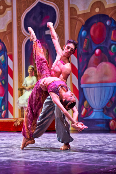 Male and female dancer in Arabian clothes perform an extension and back-bend onstage.