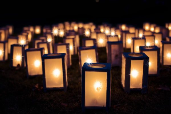 Dozens of lighted luminaria lanterns sit on the ground against a night sky