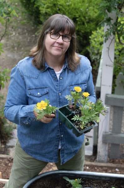 Whitney Wade in her garden with gardening gloves and a flowerin yellow plant in her hands