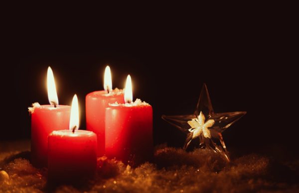 Four fat red Advent candles on a gold cloth glow against a dark background next to a glass star ornament