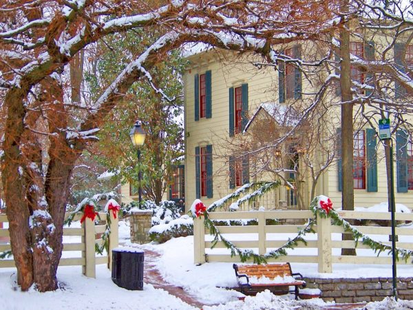 tall white building with green shutters on a snowy winter street, with oldfashioned lampposts and holly garlands with red ribobns on the fence