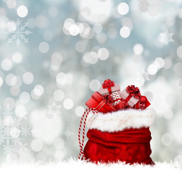 Red Santa sack, trimmed with white fur and filled iwth gifts, sits in snow against a blurred background of silver light to simulate snowflakes
