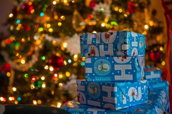 Stack of packages in blue paper printed with "Ho Ho Ho" on them in front of decorated, lighted Christmas tree