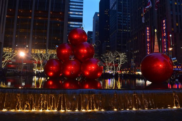 Giant red Christmas-ornament stack decoration on a New York city street, surrounded by tall buildings.