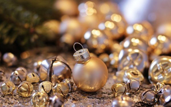 Gold Christmas ornaments and jingle bells against a background of blurred gold lights