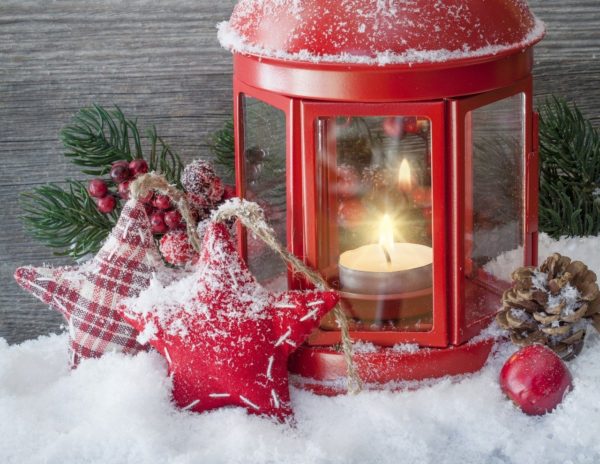Red metal lantern with white lighted tea light candle in snow next to two fabric star ornaments