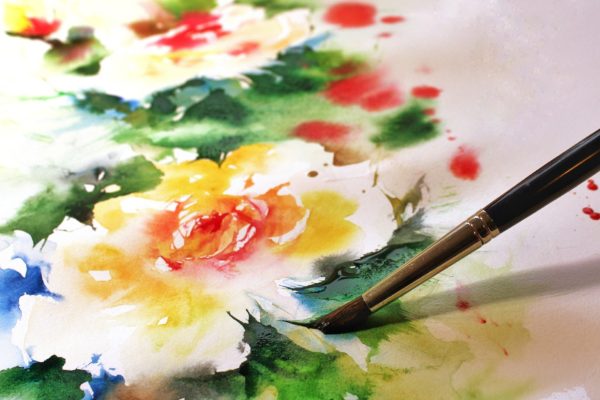 Closeup of an artist's brush painting a watercolor of flowers