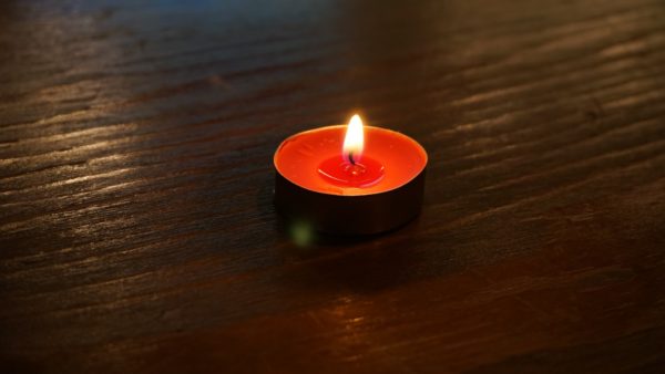 One small red tealight candle burns atop a wooden surface