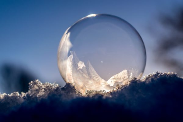 Froxen soap bubble with winglike ice patterns against a sunrise and blue sky background