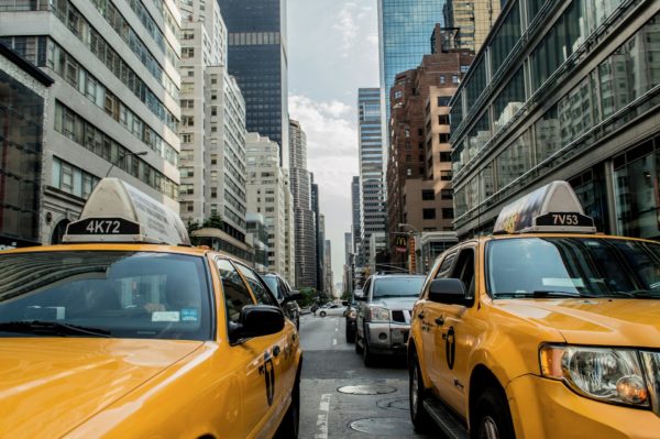 Two yellow taxis alongside each other in heavy city traffic with city buildings on either side of the street