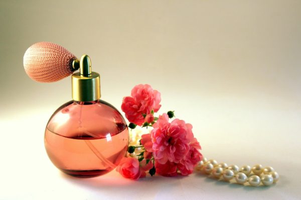 Pink cologne in an atomizer bottle on a table near string of pearls and two pink azaleas