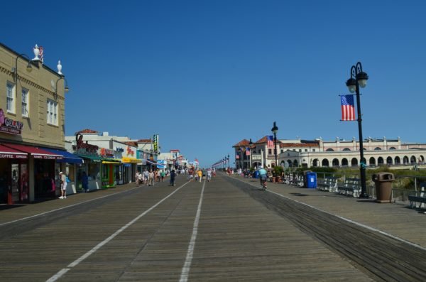 The Ocean City boardwalk, with an American flag and the Music Pier and shops against a bright blue sky