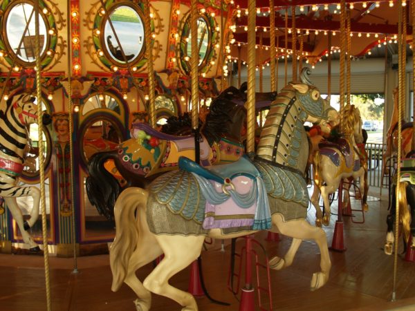 Carousel steeds including a caparisoned white horse, a zebra and a saddled black horse on a carousel with mirror panels and lit with amber lights
