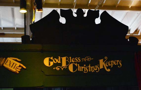 Green sign with gold lettering reads, "God bless the Christmas keepers".