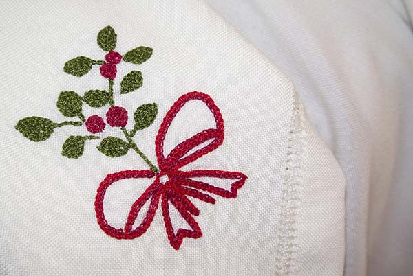 Embroidered holly with a red bow on a white napkin