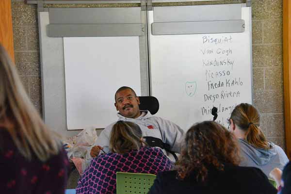 MIchael Seale Jr. teaches creativity class with two sheets of paper posted behind his wheelchair.