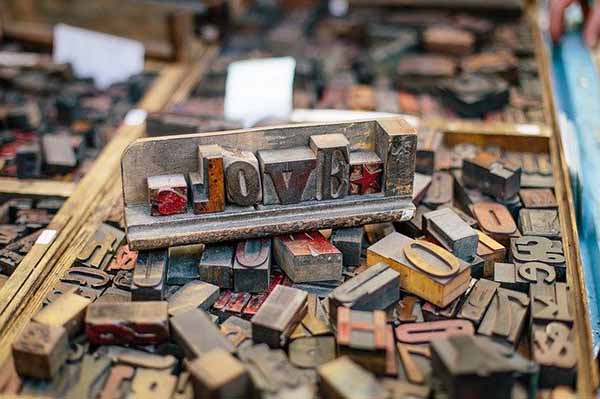 Woodtype blocks arranged on a tray to spell "LOVE" as they sit in a compartment of wood type blocks of all shapes and sizes