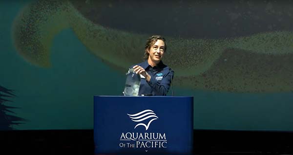 Curator of Fish and Invertebrates Janet Monday raises a glass jar of jellies from the Aquarium of the Pacific podium