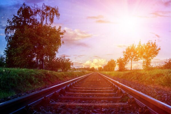 Railroad track leading away into a sunset with grass and trees on either side