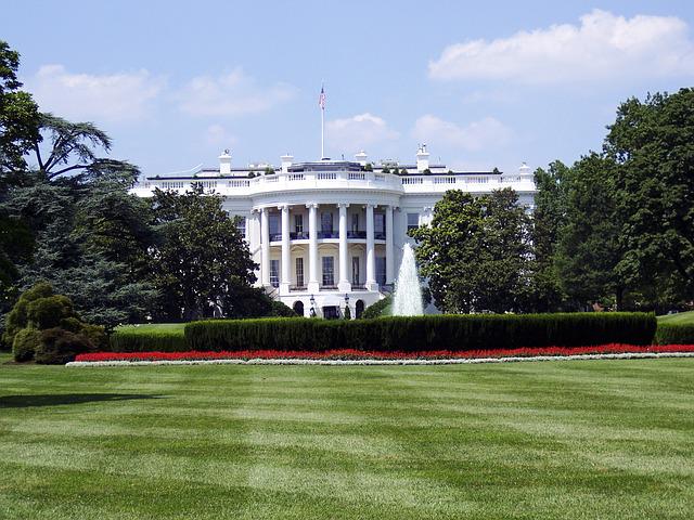 The White House sourrounded by greenery, stands behind a manicured lawn 