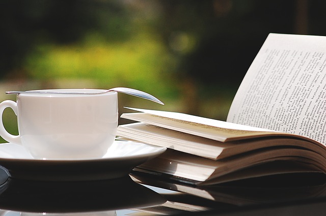 Book on an outdoor table with greenery in the background and a china cup and saucer nearby