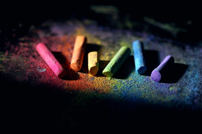 Six pieces of multicolored chalk lying in chalk dust: pink, orange yellow green, blue and purple