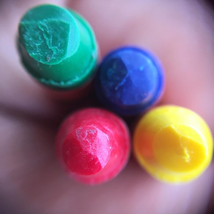 Top-down closeup of four sherbet-colored crayons: magenta, yellow aqua green and blue