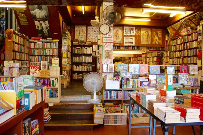 Books on bookshelves and a table in bookshop with a clock on the wall