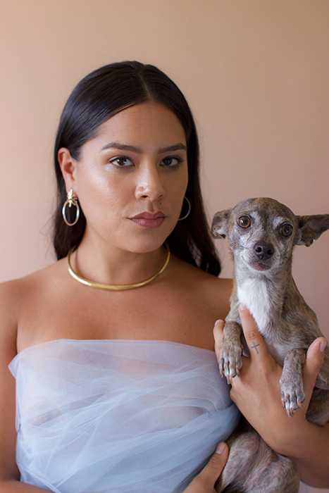 Jessica Linahan, wearing hoop earrings and a gold choker necklace, poses with her dog.