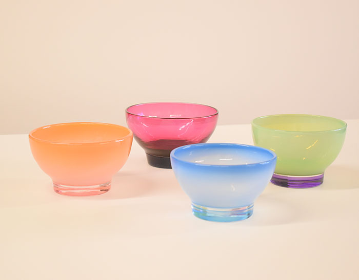 Four translucent glass bowls--orange, red, blue, and green--on a counter