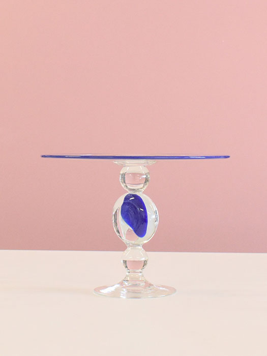 Tall glass pedestal cake stand with blue plate and blue in its clear pedestal.