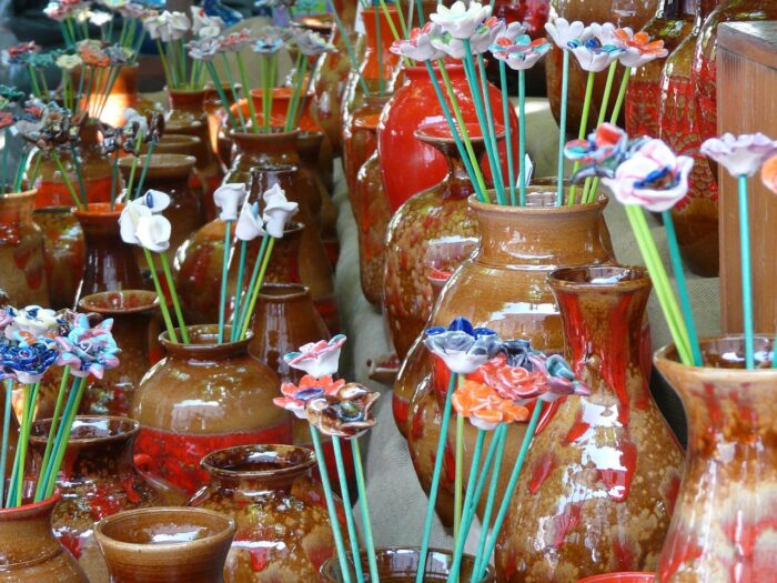 Colorful ceramic daisies, rose and lilies stand in tall brown glazed pottery jugs at outdoor crafts fair.