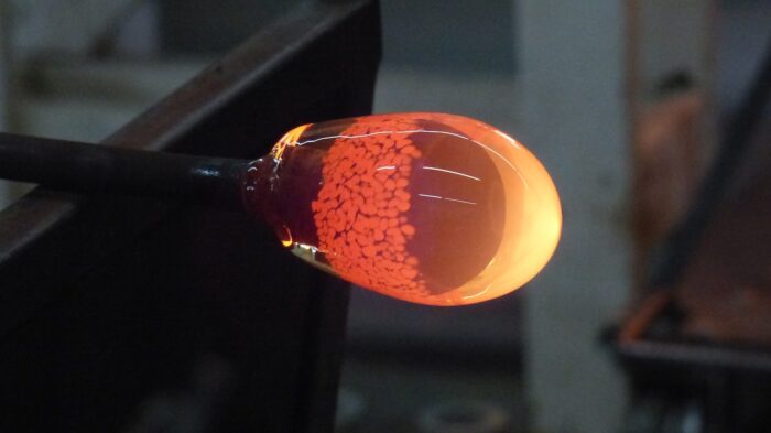 Red-hot molten glass glows orange at the end of a rod.