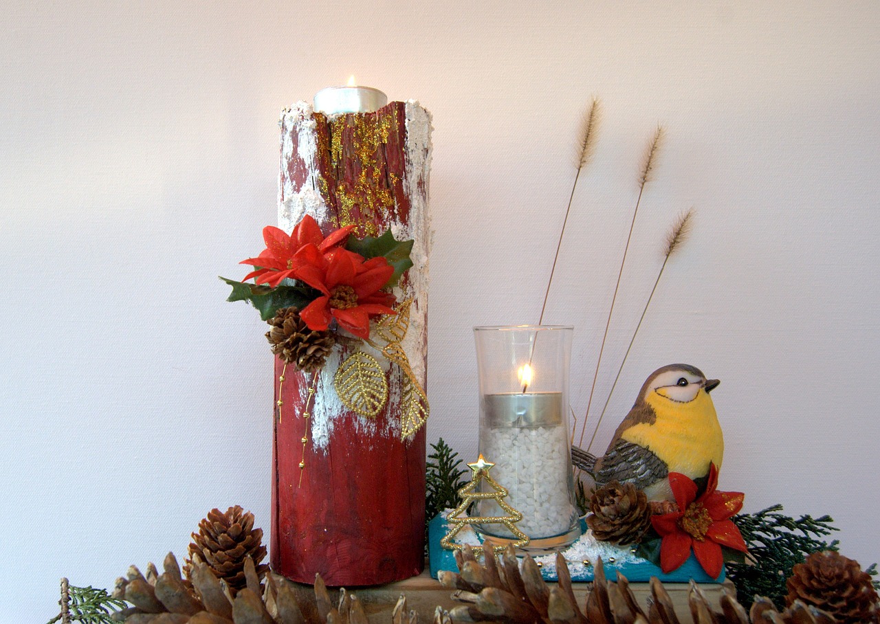 White birch log with candles and red poinsettias sits in a greenery arrangement with a painted goldfinch on a table