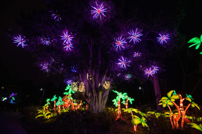 Twinkling purple stars in a lighted tree with lush green LED lighted foliage in the distance