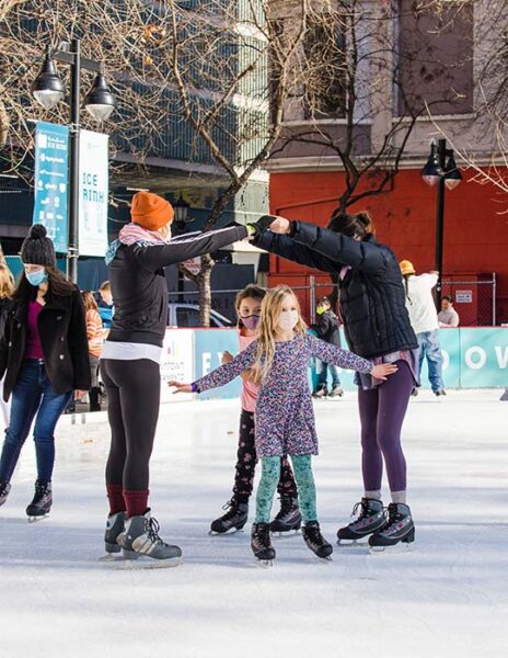 Parents hold their arms in a bridge-like "arch" for two small children to skate under.