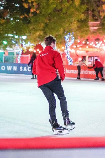 Man in a red jacket skates expertly on the ice of the lit-up rink.