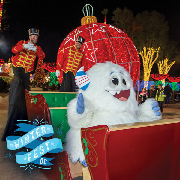 A grinning Yowie the Yeti sits in a red sleigh against a backgrounf with a red Christmas ornament and toy soldier, with "Winter Fest OC" on a blue streamer in the lower left of the picture