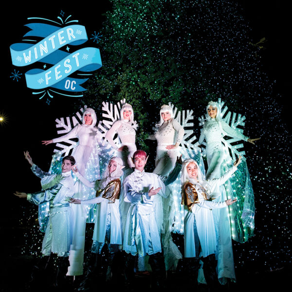 Christmas sprites and elves in white costumes with lights group in a circle with "Winterfest OC" on a blue banner in the upper left corner of the picture