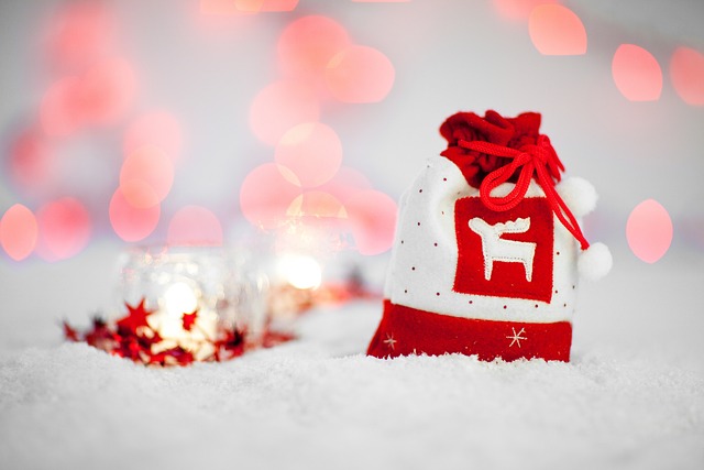 Red-and-white felt drawstring gift bag with a white reindeer on it in snow with white votive candles nearby
