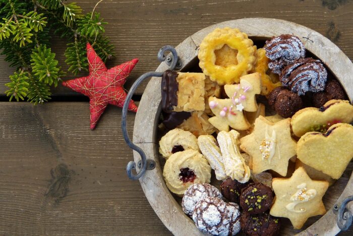 Plate of a variety of Christmas cookies including heart-shaped jelly filled sugar cutouts, chocolate "snowballs" and star-shaped butter cookies with white icing highlights, on a plate next to a red star ornament and greenery