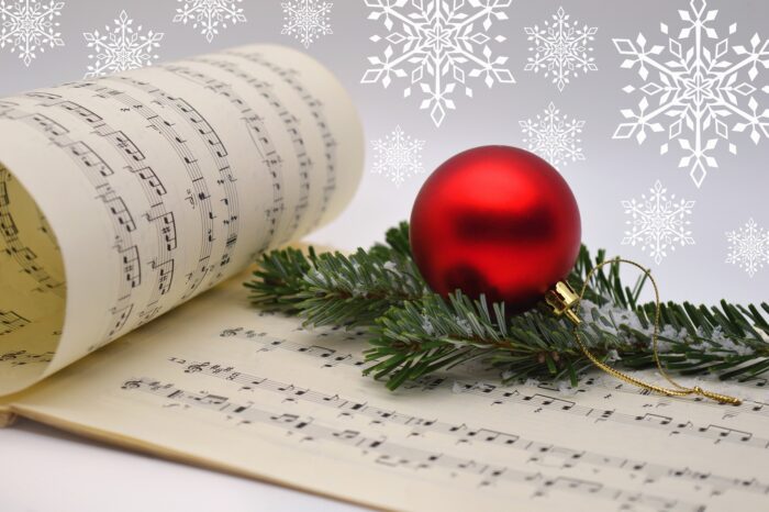 Red Christmas ornament and pine bough atop a musical score with white snowflakes against a silver background