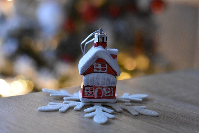 Small glass cottage Christmas ornament stands in the center of a wooden snowflake, painted white, on a surface.
