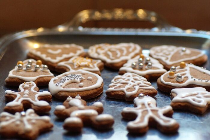 Tray of cutout gingerbread cookies including gingerbread people trees and hears, decorated in white icing.