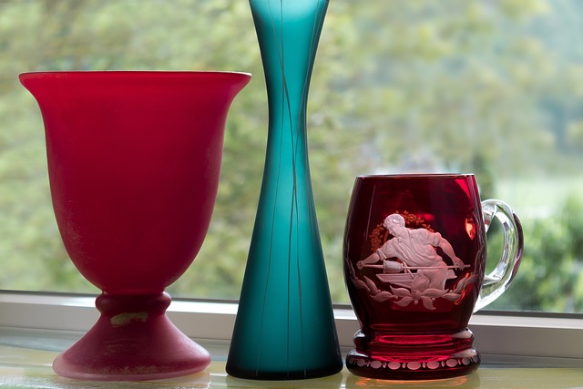 Three handblown glass items: a red wide vase, a slim green bud vase and a burgundy mug etched with the figure of a man