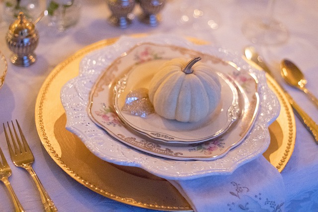 Thanksgiving place setting with a gold large plate beneath three smaller white plates, gradually decreasing in size, with a miniature white pumpkin on the smallest