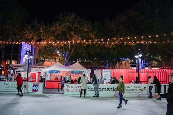 Skaters on the rink at night against a background of lit-up special-event tents