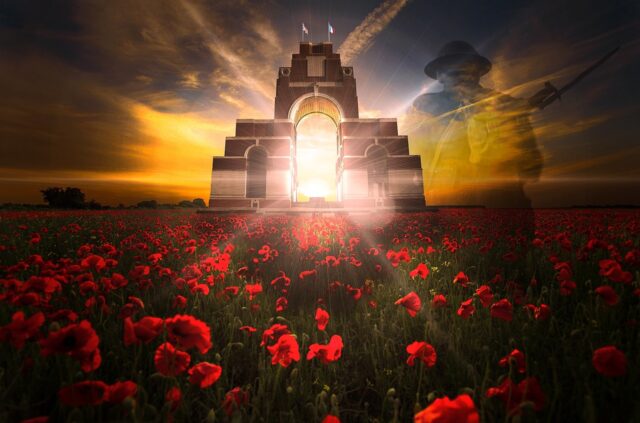 Archway of a memorial against a sunset in a field of poppies whith a shadowy figure of a soldier near it